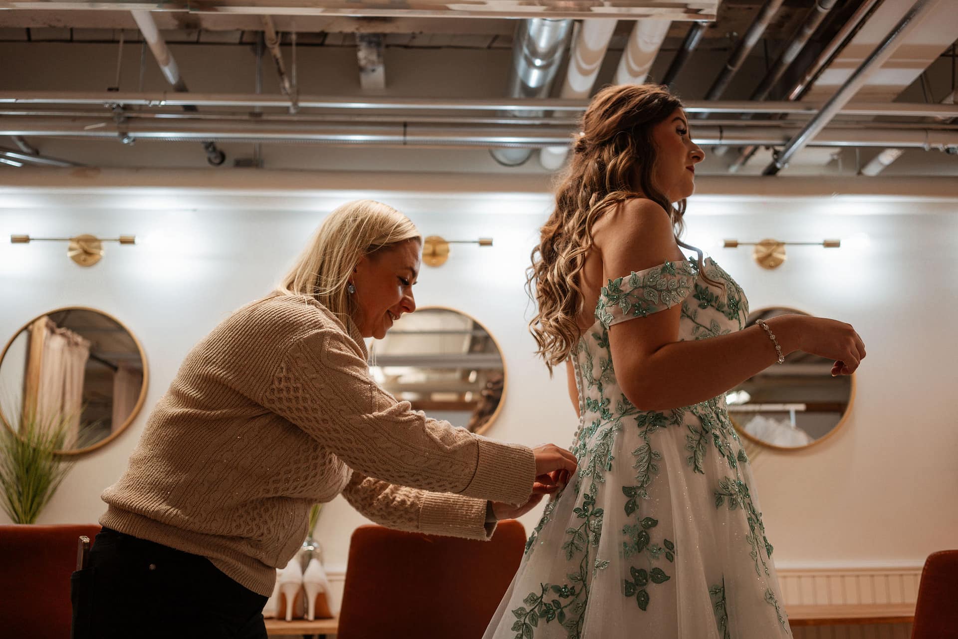 woman helping bride attach greenery details to wedding dress